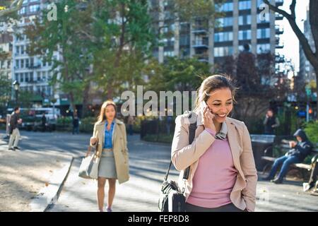 Giovane donna parlando sullo smartphone mentre a piedi attraverso il parco della città Foto Stock