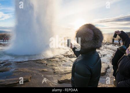 Donna di fotografare il grande Geysir, un geyser nella valle di Haukadalur sulle pendici della collina Laugarfjall, nel sud-ovest dell'Islanda Foto Stock