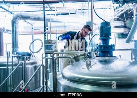 Giovane uomo in birreria indossando grembiuli e guanti protettivi di birra di test nel serbatoio Foto Stock