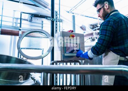 Giovane uomo in birreria indossando grembiuli e guanti di protezione utilizzando lo schermo a sfioramento delle apparecchiature informatiche Foto Stock