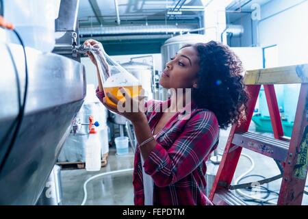 Giovane donna in birreria pallone di riempimento con la birra dal serbatoio di fermentazione Foto Stock