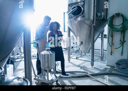 I colleghi nella birreria conica dal serbatoio di fermentazione di fianco a fianco guardando a tavoletta digitale Foto Stock