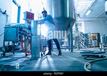 Basso angolo vista laterale del giovane uomo in birreria conica dal serbatoio di fermentazione di collegare tubo flessibile per taniche Foto Stock