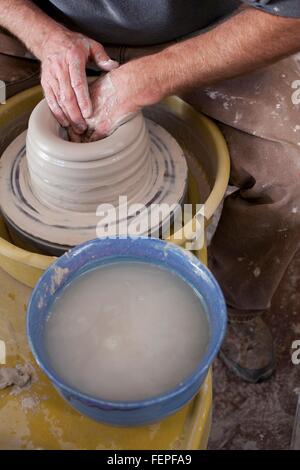 Ritagliata ad alto angolo di visione dei vasai mani sagomatura di pentola di creta sulla ruota in ceramica Foto Stock