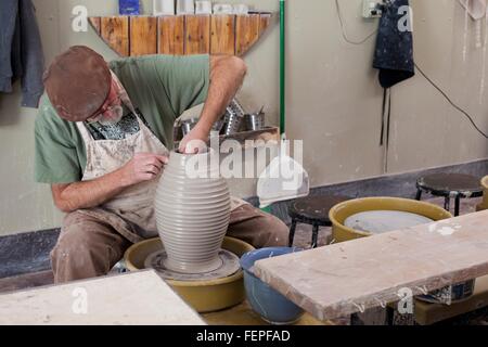 Potter indossando il tappo piatto seduti al volante di ceramiche di sagomatura vaso di creta Foto Stock