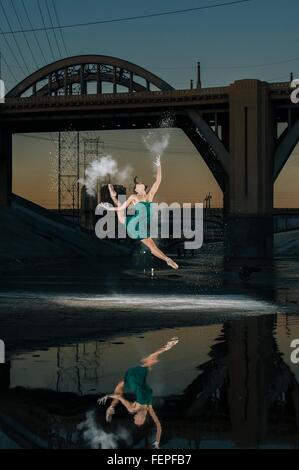 Femmina danzatore di balletto saltando mentre il rilascio di esplosione della polvere sopra il fiume al tramonto, Los Angeles, Stati Uniti d'America Foto Stock