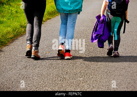 Vista posteriore di tre persone a piedi lungo una strada di campagna che indossa scarponi e scarpe da ginnastica Foto Stock