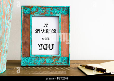 Vintage photo frame su un tavolo di legno oltre il muro bianco lo sfondo con il messaggio motivazionale COMINCIA CON VOI Foto Stock