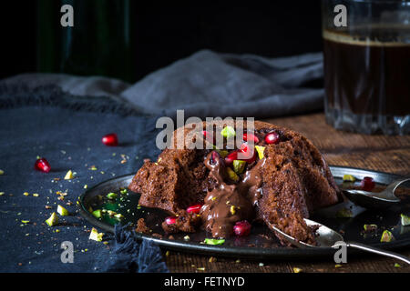 Lava di cioccolato torta decorata con un trito di pistacchi e i semi di melograno. Tazza di caffè nero a parte. Rustico sfondo di legno Foto Stock