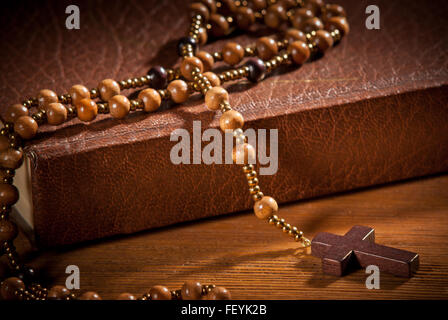 Il libro chiuso con rosario sulla scrivania in legno Foto Stock