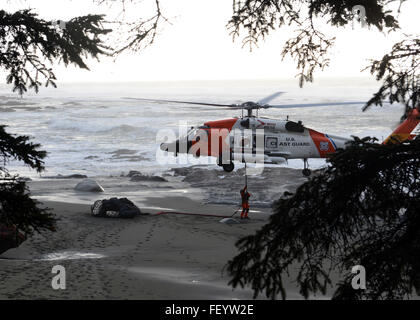 Petty Officer di terza classe Michael Tate, aviazione un tecnico di manutenzione presso la guardia costiera Stazione aria Astoria, ganci fino a rete piena di spiaggia detriti e rifiuti al fondo di un MH-60 Jayhawk elicottero a una spiaggia vicino a Neah Bay, nello Stato di Washington, 22 gennaio 2015. I detriti e la sporcizia è stato scaricato nei dintorni di carrelli elevatori per ulteriore smaltimento. Foto Stock