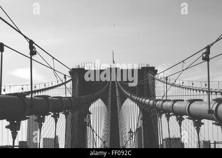 Una vista in bianco e nero del Ponte di Brooklyn a New York City, con la bandiera americana ben visibile. Il ponte sospeso attraversa l'East River, offrendo una vista iconica e storica della città. Foto Stock