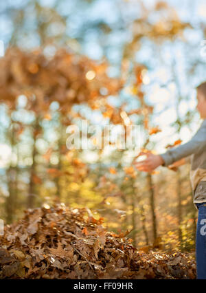 Un bambino gioca con gioia con foglie essiccate in un ambiente esterno. Le vivaci foglie arancioni e marroni sono sparse per terra, a simboleggiare la bellezza dell'autunno. Foto Stock