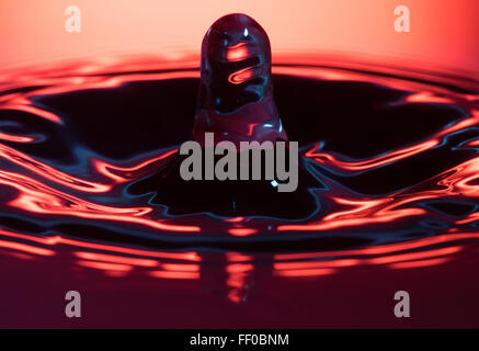 Una goccia di acqua che colpisce la superficie di un contenitore pieno di liquido Foto Stock