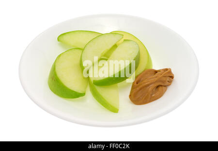 Un gruppo di mela verde le fette su un piatto con una piccola quantità di burro di arachidi per immersione isolato su uno sfondo bianco. Foto Stock