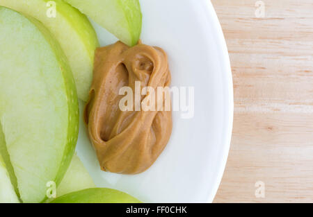 Top vista ravvicinata di un gruppo di mela verde le fette su un piatto con una piccola quantità di burro di arachidi per immersione su una tavola di legno top Foto Stock