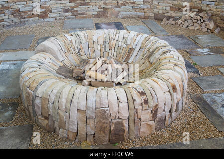 Giardino con una buca circolare di fuoco fatta di pietra in una ghiaia e pietra pavimentata area patio UK Foto Stock