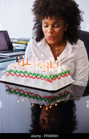 Persona d'affari Celebrando 28 anni e facendo un partito in ufficio. Ella si brucia il clandles sulla torta di compleanno e sorrisi di gioia Foto Stock