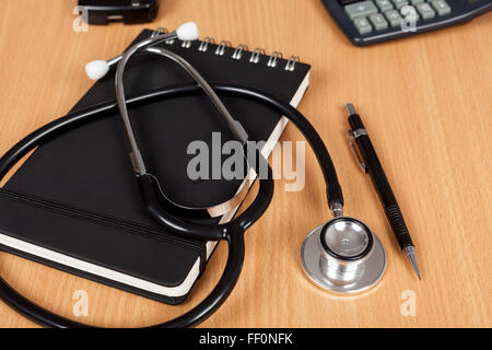 I medici lo stetoscopio posa su un blocco note su una scrivania con una penna e una calcolatrice Foto Stock