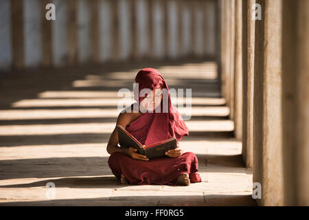 Un giovane monaco di lettura con raggi di sole e in templi di Bagan, Myanmar Foto Stock