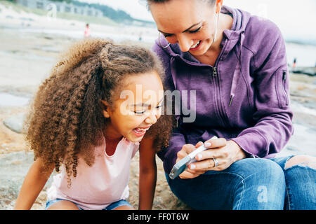 Madre e figlia tramite telefono cellulare sulla spiaggia