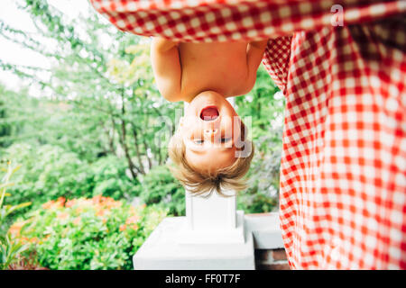 Baby boy appeso a testa in giù all'aperto Foto Stock