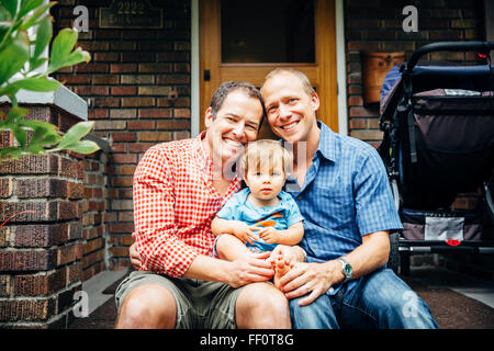Gay padri holding baby figlio sulla parte anteriore stoop Foto Stock