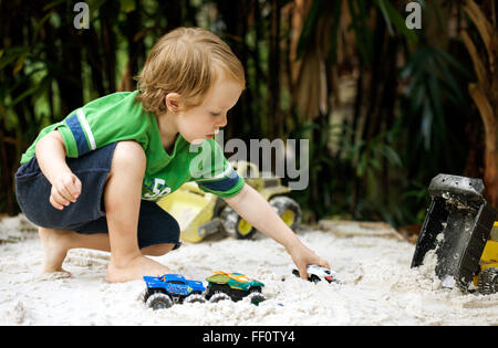 Un giovane ragazzo gioca con carrelli in una sandbox all'esterno. Foto Stock