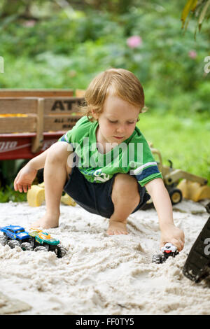 Un giovane ragazzo gioca con carrelli in una sandbox all'esterno. Foto Stock