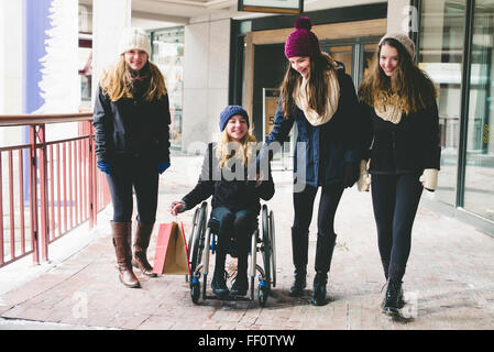 Le ragazze a piedi e tramite sedia a rotelle sul marciapiede Foto Stock