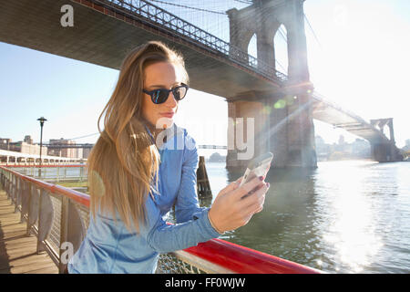 La donna caucasica tramite telefono cellulare sul lungomare, New York New York, Stati Uniti Foto Stock