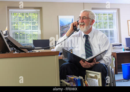 Imprenditore caucasico parlando al telefono alla scrivania Foto Stock