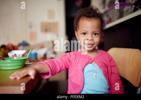 Razza mista baby ragazza seduta a tavola Foto Stock