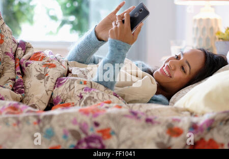 Razza mista donna tramite telefono cellulare a letto Foto Stock