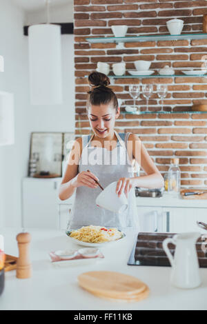 La donna caucasica versando in salsa di pasta in cucina Foto Stock