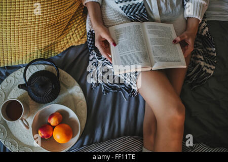 Donna che legge un libro sul letto Foto Stock