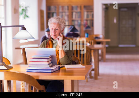 I vecchi razza mista donna utilizzando laptop in biblioteca Foto Stock