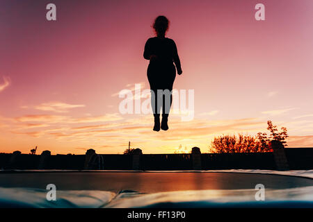 Silhouette di belle dimensioni più giovane ragazza di saltare sul trampolino sulla sera Cielo blu sullo sfondo Foto Stock