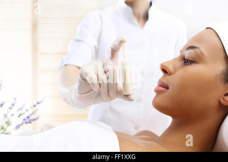 Fiala cosmetica, siero applicato al viso di una donna . Estetiste mano mostra una fiala con una preparazione cosmetica Foto Stock