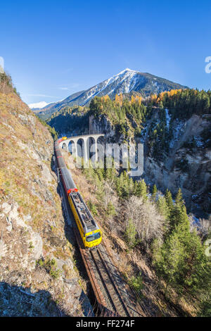 Bernina Express passa al di sopra del Landwasser Viadukt circondato da boschi colorati del Cantone dei Grigioni, Svizzera, Europa Foto Stock