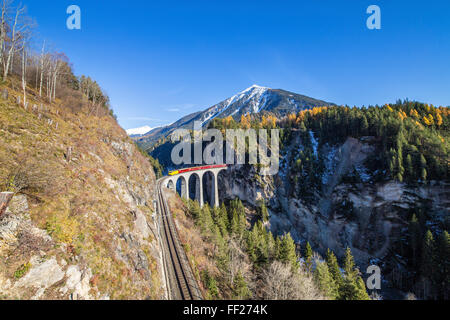 Bernina Express passa al di sopra del Landwasser Viadukt circondato da boschi colorati del Cantone dei Grigioni, Svizzera, Europa Foto Stock