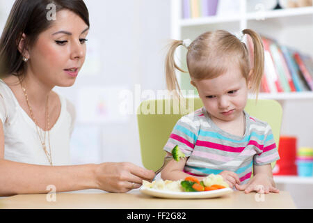 Bambino bambina guarda con disgusto per ortaggi sani. Madre convince la figlia a mangiare cibo. Foto Stock