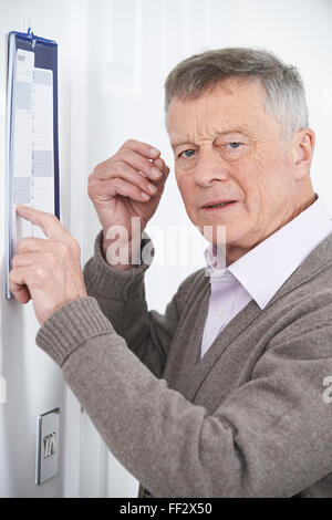 Confuso uomo anziano con demenza guardando il calendario da parete Foto Stock