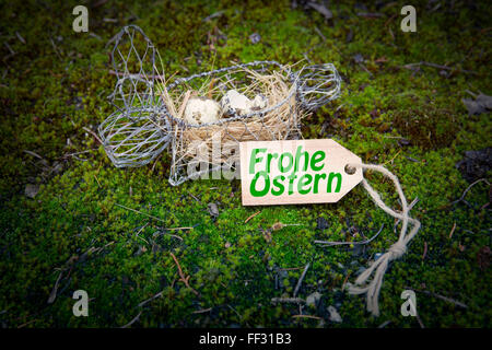 I tedeschi 'Frohe Ostern' (Felice Pasqua) sul tag di legno con il coniglietto di pasqua cesto su verde muschio Foto Stock