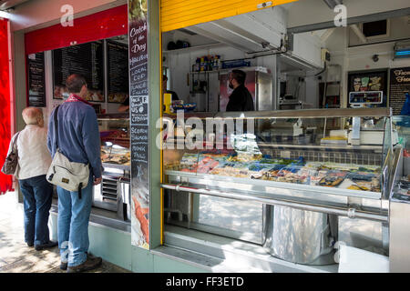 Due clienti per un pescivendolo stallo in luogo di mercato, Norwich, Norfolk, Regno Unito Foto Stock