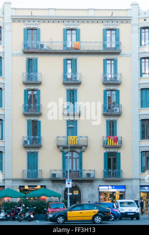 Facciata di un edificio a Barcellona con un taxi alla porta e bandiere nazionalista al balcone Foto Stock