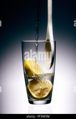L'acqua versata in un bicchiere di limoni Foto Stock
