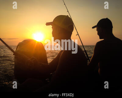 Silhouette di due giovani uomini la pesca al tramonto ora dalla parte posteriore della loro imbarcazione Foto Stock
