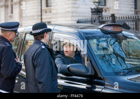 Londra, Regno Unito. Il 10 febbraio 2016. Un black cab taxi driver parla di funzionari di polizia al di fuori di Downing Street durante un go-slow protesta a Whitehall contro la mancanza di controllo da parte del governo di minicab Uber app. Credito: Mark Kerrison/Alamy Live News Foto Stock