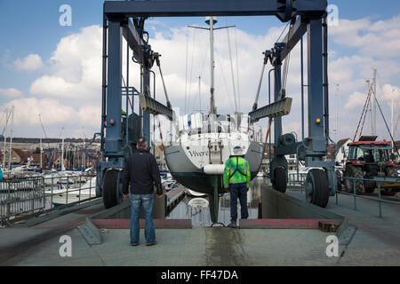 Il proprietario si affaccia su come il suo yacht di grandi dimensioni è lanciato in acqua in un marina supportato da una barca culla ascensore. Foto Stock